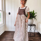 Brown washed denim overall top with silver metal hardware and adjustable straps and a cream and brown striped, lightweight skirt with pockets.