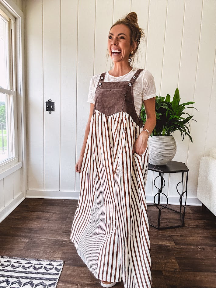 Brown washed denim overall top with silver metal hardware and adjustable straps and a cream and brown striped, lightweight skirt with pockets.