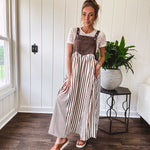 Brown washed denim overall top with silver metal hardware and adjustable straps and a cream and brown striped, lightweight skirt with pockets.