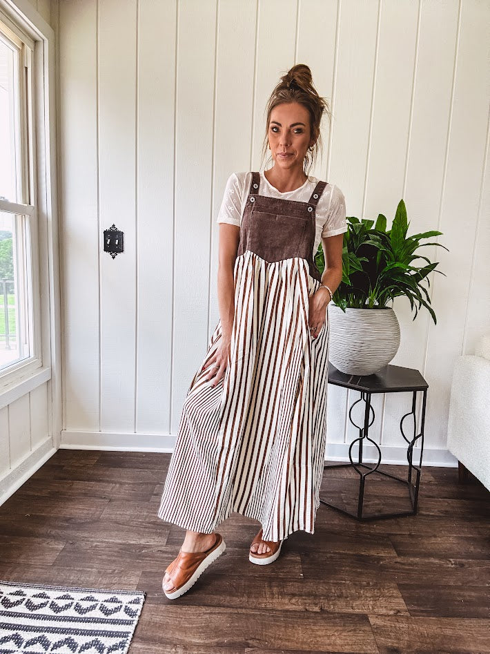Brown washed denim overall top with silver metal hardware and adjustable straps and a cream and brown striped, lightweight skirt with pockets.