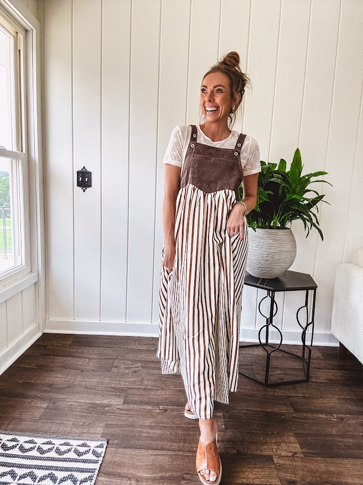Brown washed denim overall top with silver metal hardware and adjustable straps and a cream and brown striped, lightweight skirt with pockets.