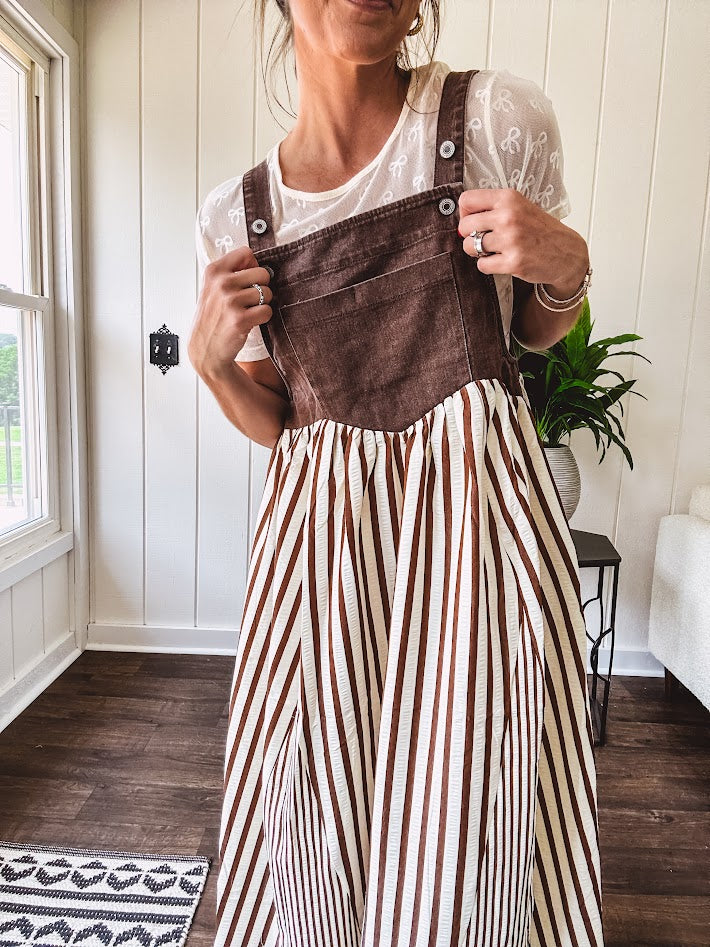 Brown washed denim overall top with silver metal hardware and adjustable straps and a cream and brown striped, lightweight skirt with pockets.