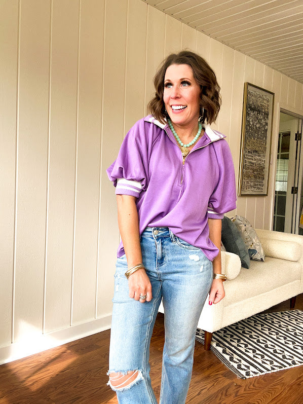 Soft, orchid 1/4 zip top with short sleeves and white striped trim at the collar and elastic sleeves. Loose hem.