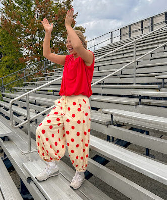 Soft, stretchy cream elastic drawstring waist pants with large red polka dots throughout, pockets and button cuffs for a balloon-like silhouette.