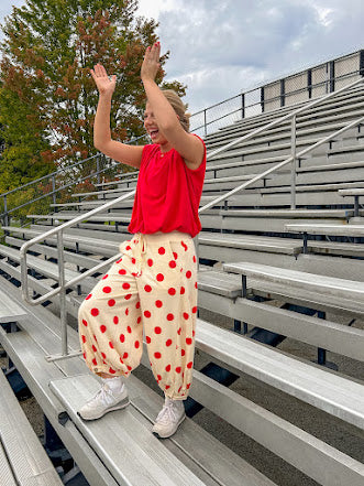 Soft, stretchy cream elastic drawstring waist pants with large red polka dots throughout, pockets and button cuffs for a balloon-like silhouette.