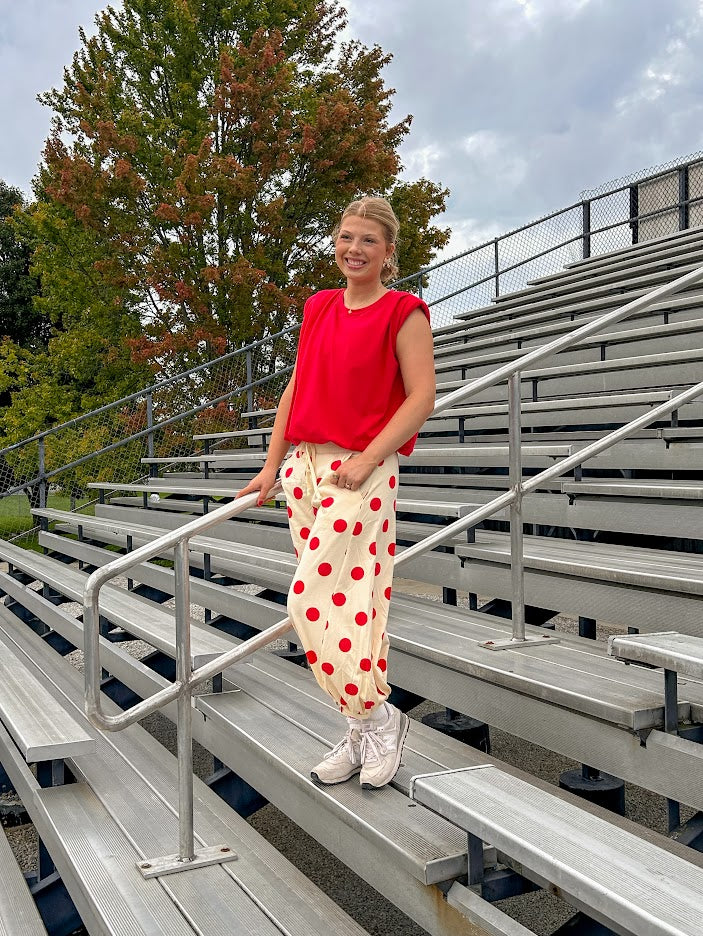 Soft, stretchy cream elastic drawstring waist pants with large red polka dots throughout, pockets and button cuffs for a balloon-like silhouette.
