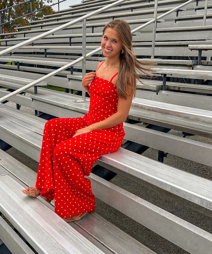 Red jumpsuit with white polka dots throughout, adjustable, removable spaghetti straps, wide leg design and cutout at the back.