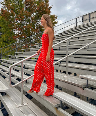 Red jumpsuit with white polka dots throughout, adjustable, removable spaghetti straps, wide leg design and cutout at the back.