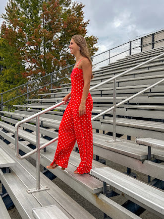 Red jumpsuit with white polka dots throughout, adjustable, removable spaghetti straps, wide leg design and cutout at the back.