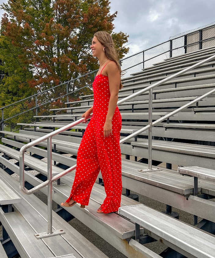 Red jumpsuit with white polka dots throughout, adjustable, removable spaghetti straps, wide leg design and cutout at the back.
