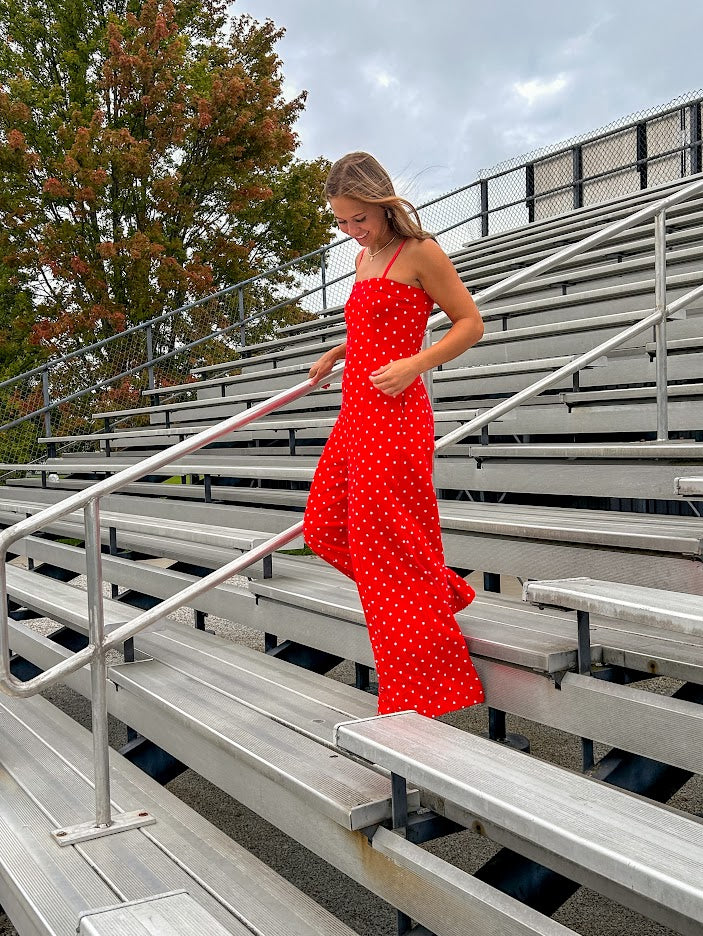 Red jumpsuit with white polka dots throughout, adjustable, removable spaghetti straps, wide leg design and cutout at the back.