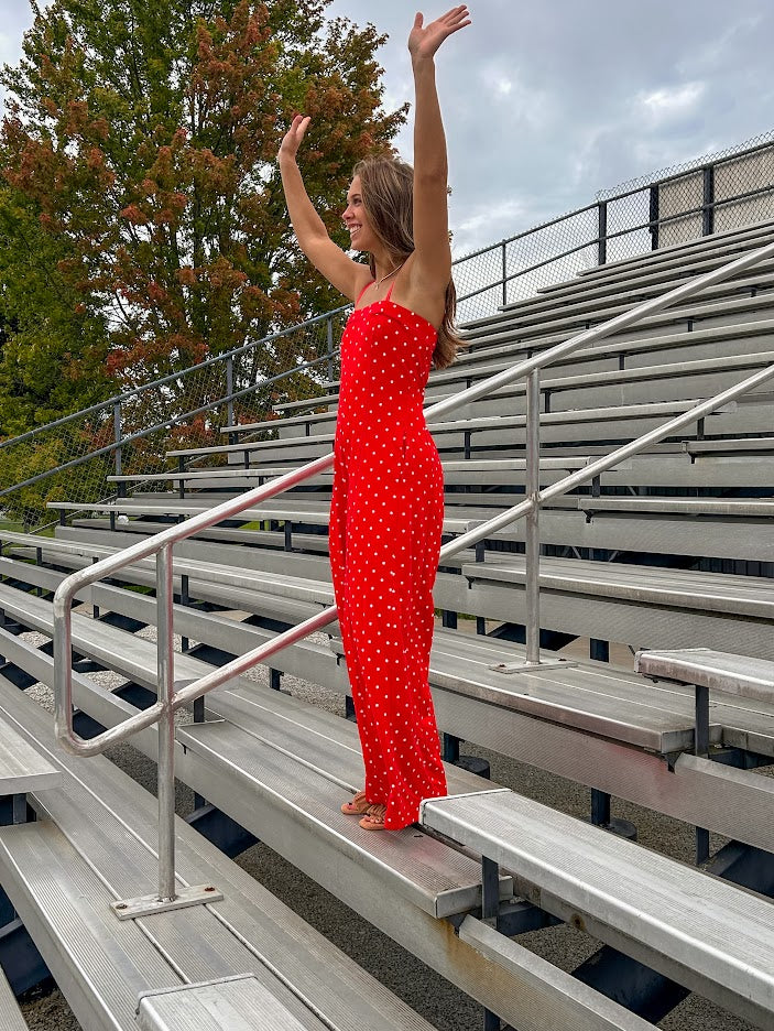 Red jumpsuit with white polka dots throughout, adjustable, removable spaghetti straps, wide leg design and cutout at the back.