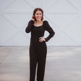 Black silky jumpsuit with puffed long sleeves, square neckline, side cutouts, elastic at the back waist and a tie at the back neckline.