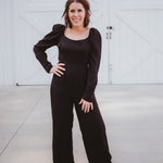 Black silky jumpsuit with puffed long sleeves, square neckline, side cutouts, elastic at the back waist and a tie at the back neckline.
