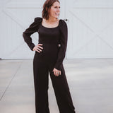 Black silky jumpsuit with puffed long sleeves, square neckline, side cutouts, elastic at the back waist and a tie at the back neckline.