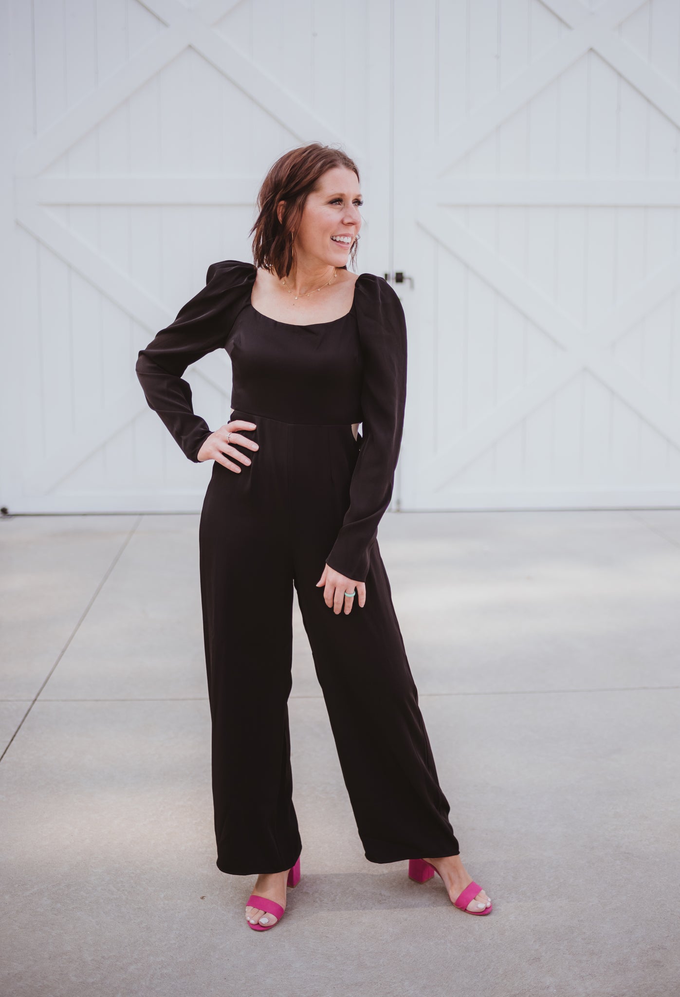 Black silky jumpsuit with puffed long sleeves, square neckline, side cutouts, elastic at the back waist and a tie at the back neckline.