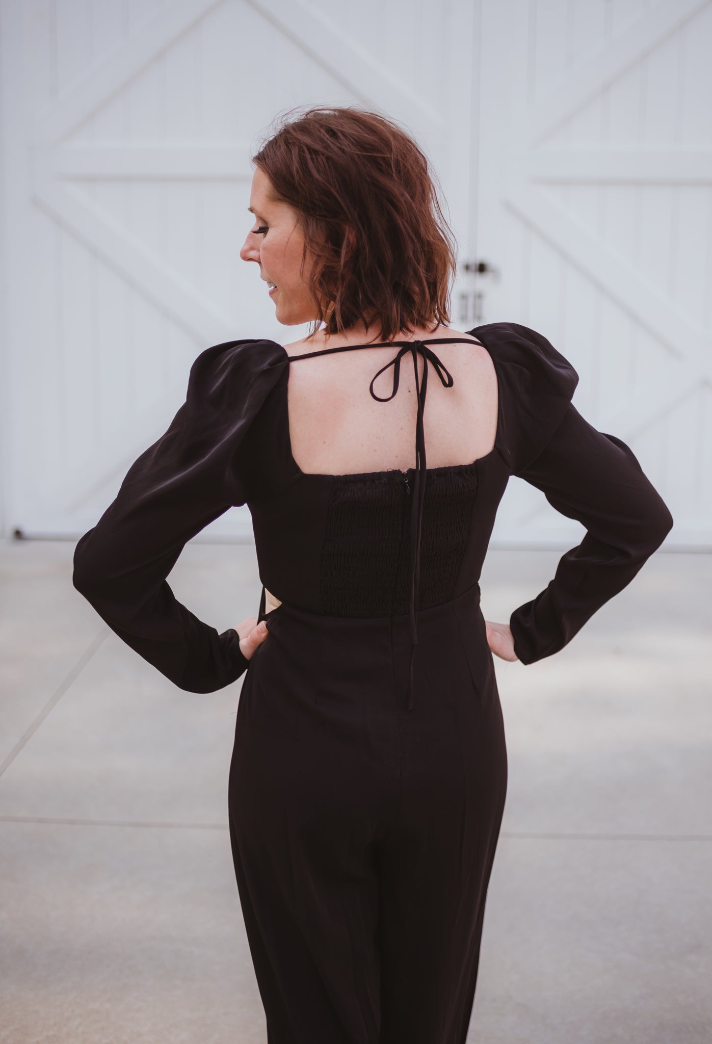 Black silky jumpsuit with puffed long sleeves, square neckline, side cutouts, elastic at the back waist and a tie at the back neckline.